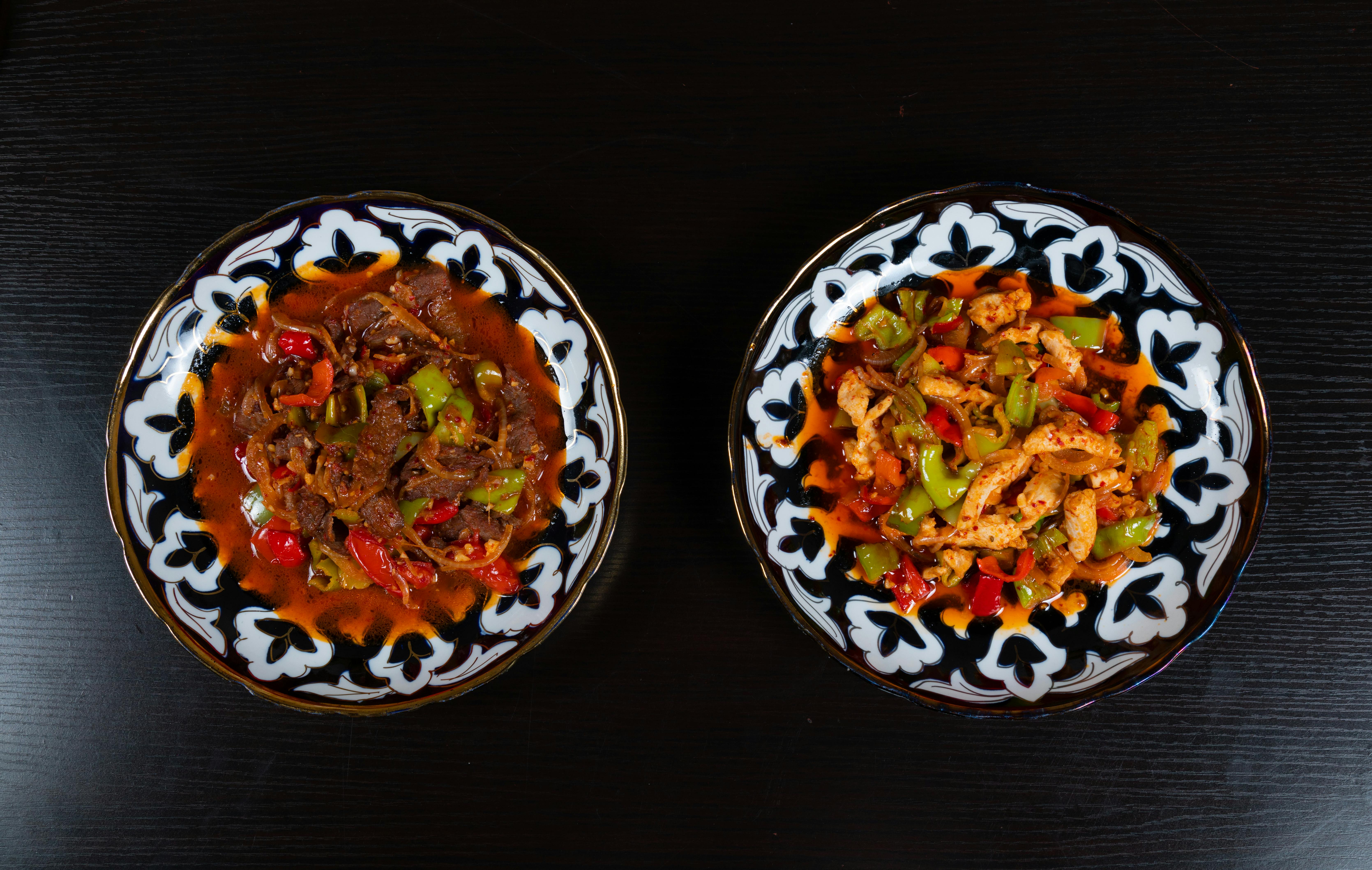 Two traditional spicy beef and chicken dishes served on decorative plates with a dark background.