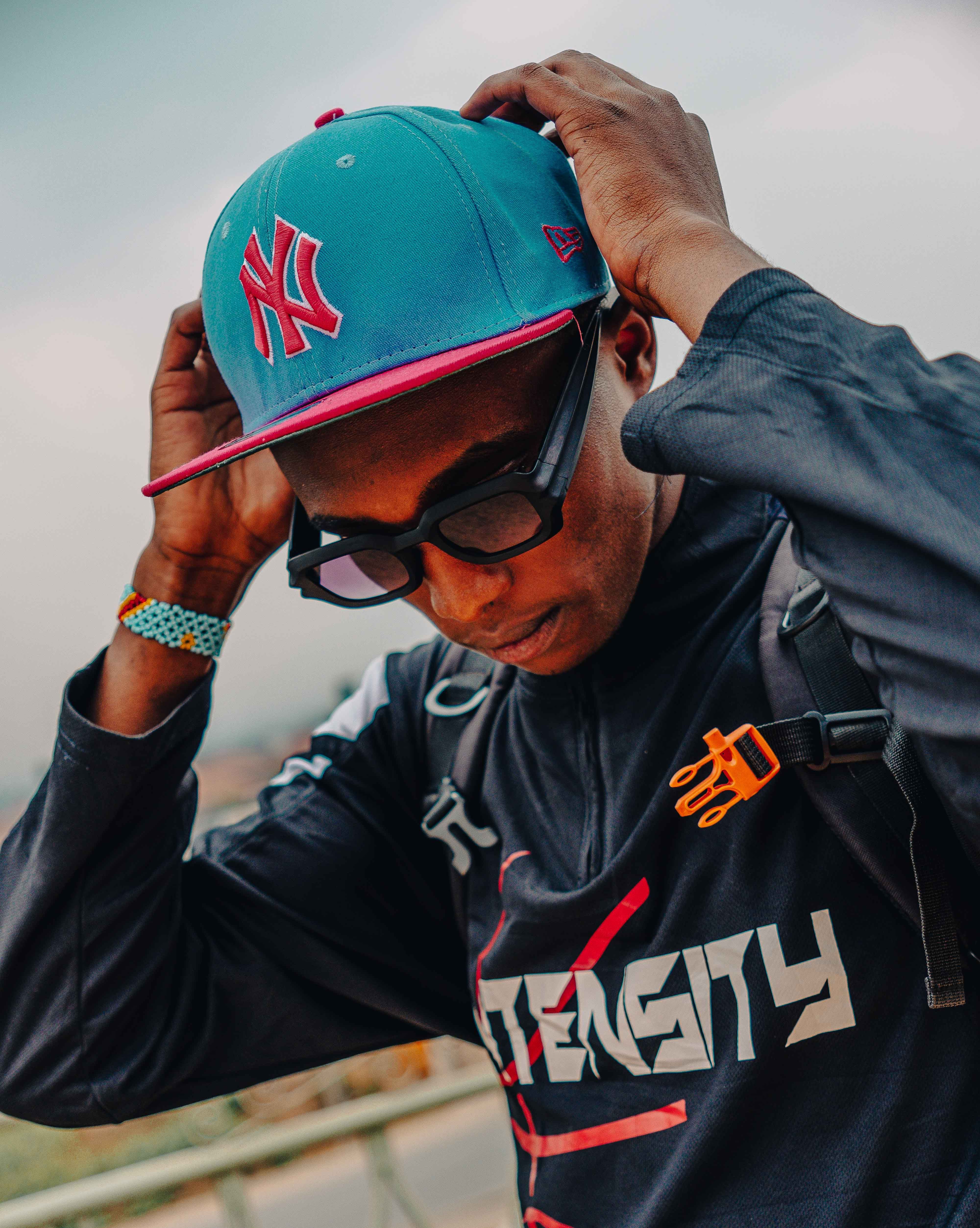 Young man wearing a cap and sunglasses adjusting accessories outdoors.