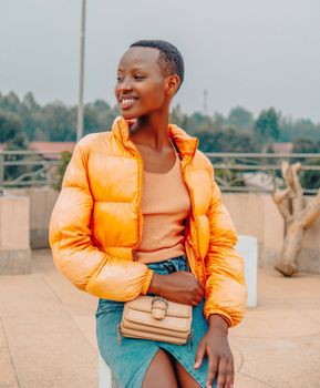 Young woman in vibrant orange jacket enjoying a sunny day outdoors.