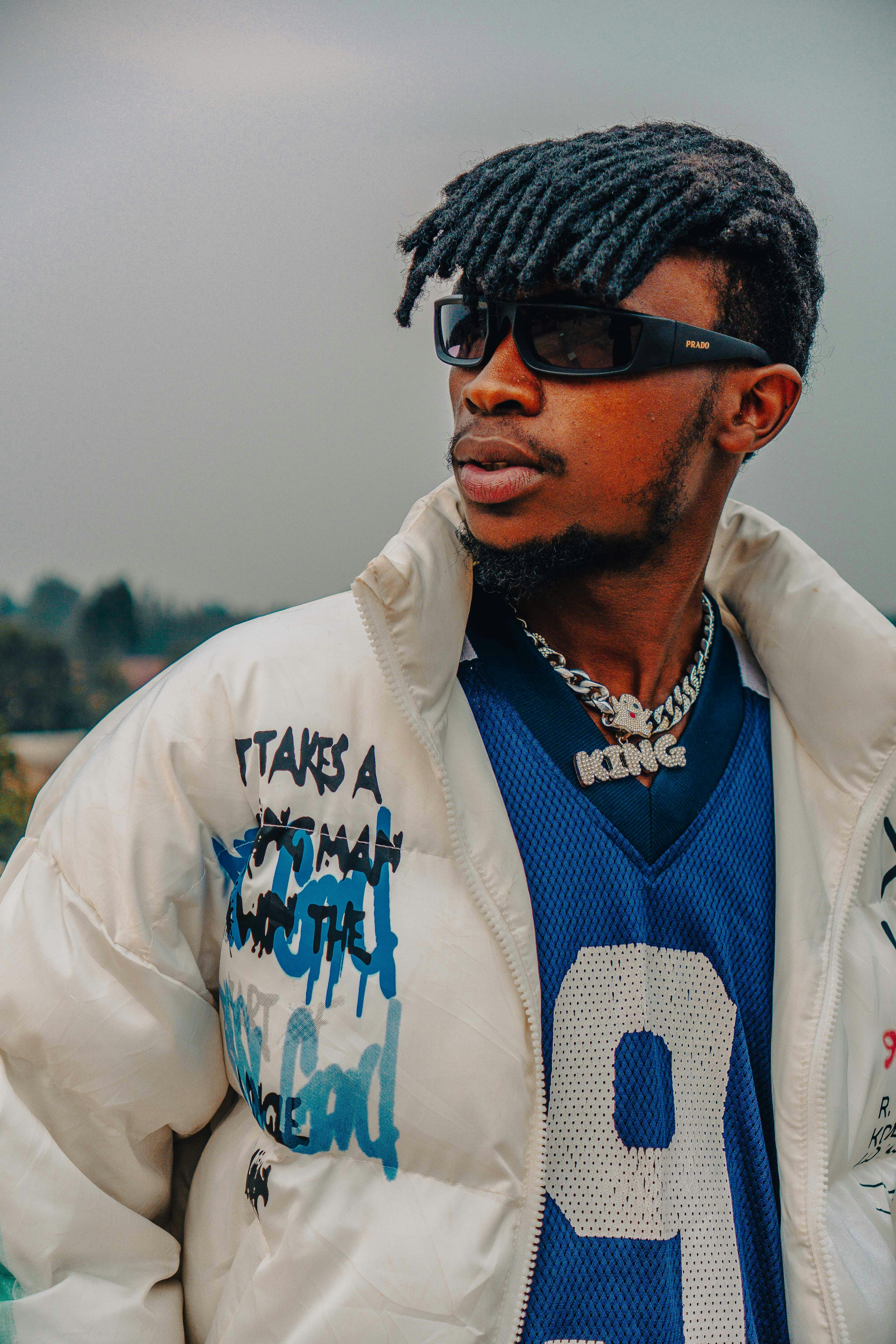 Fashionable man wearing sunglasses and a chain, posing confidently outdoors.