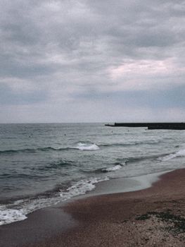 An atmospheric view of the ocean with a cloudy sky and gentle waves on a serene beach.