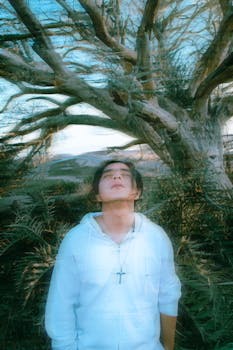A man in white gazes upwards amidst a mystical tree setting in Tijuana, Mexico.