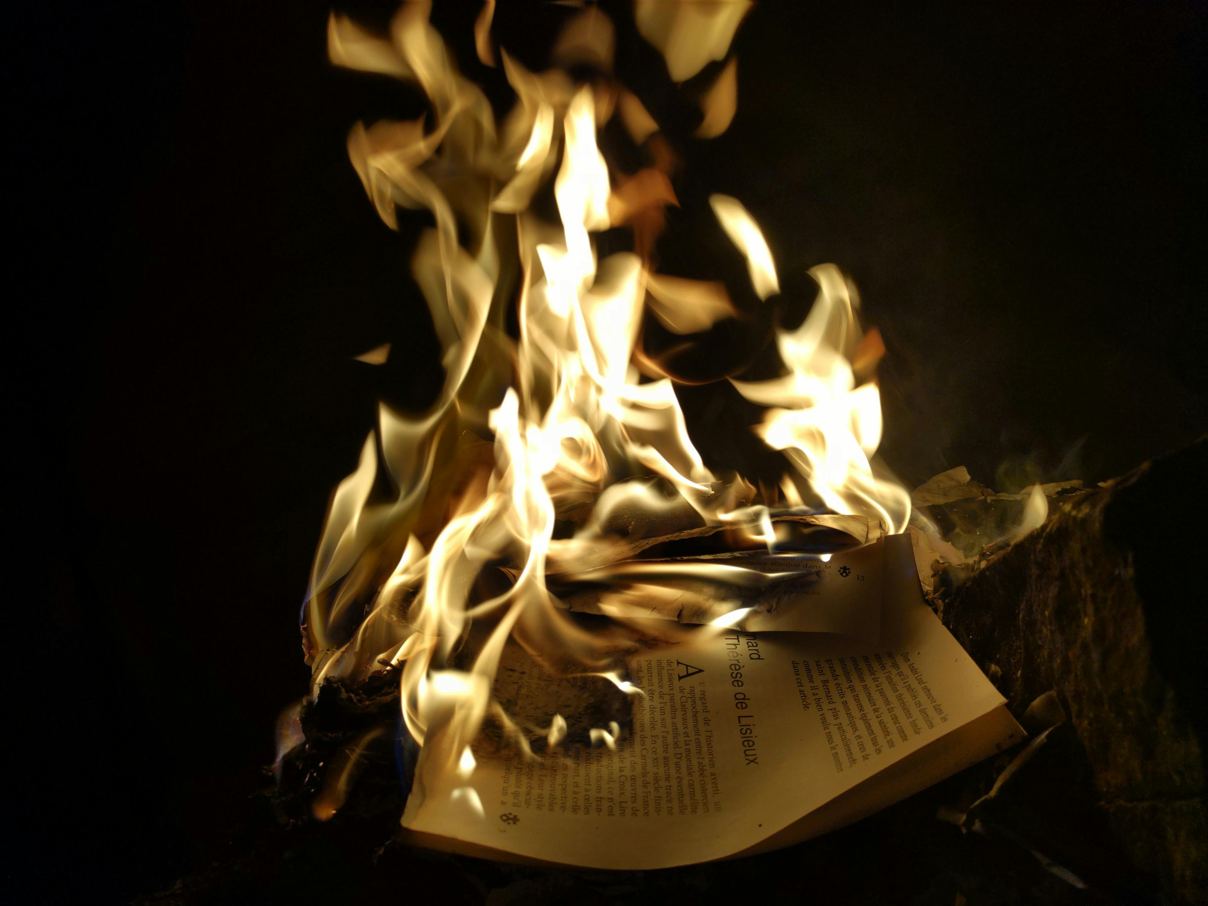 A dramatic close-up of burning pages with intense flames in a dark setting.