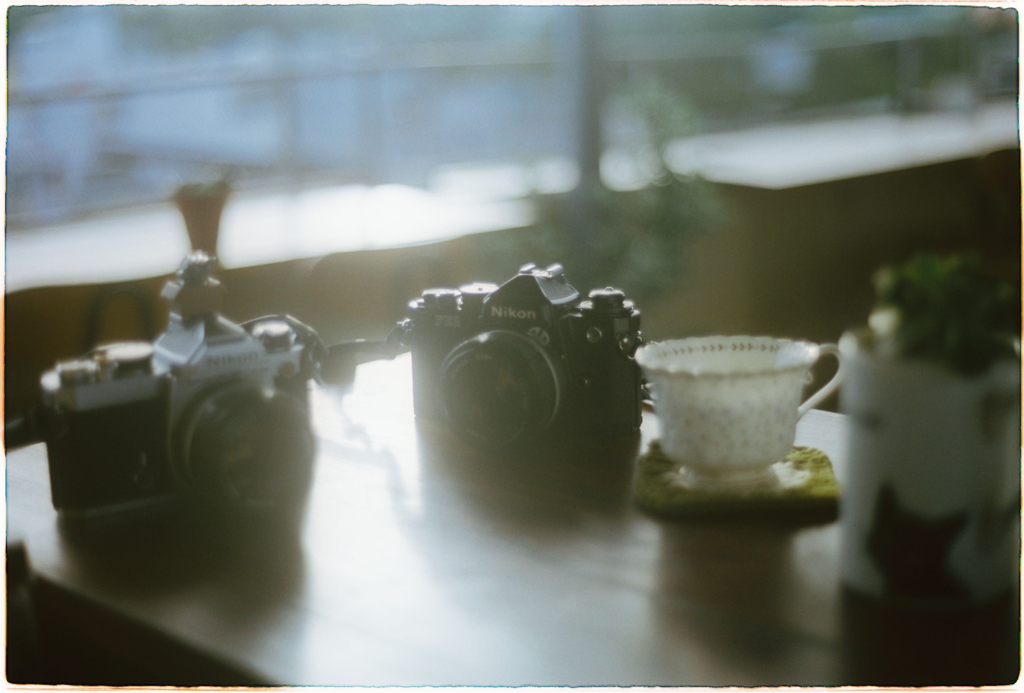 A nostalgic scene featuring vintage cameras and a tea cup on a table with soft, warm lighting.