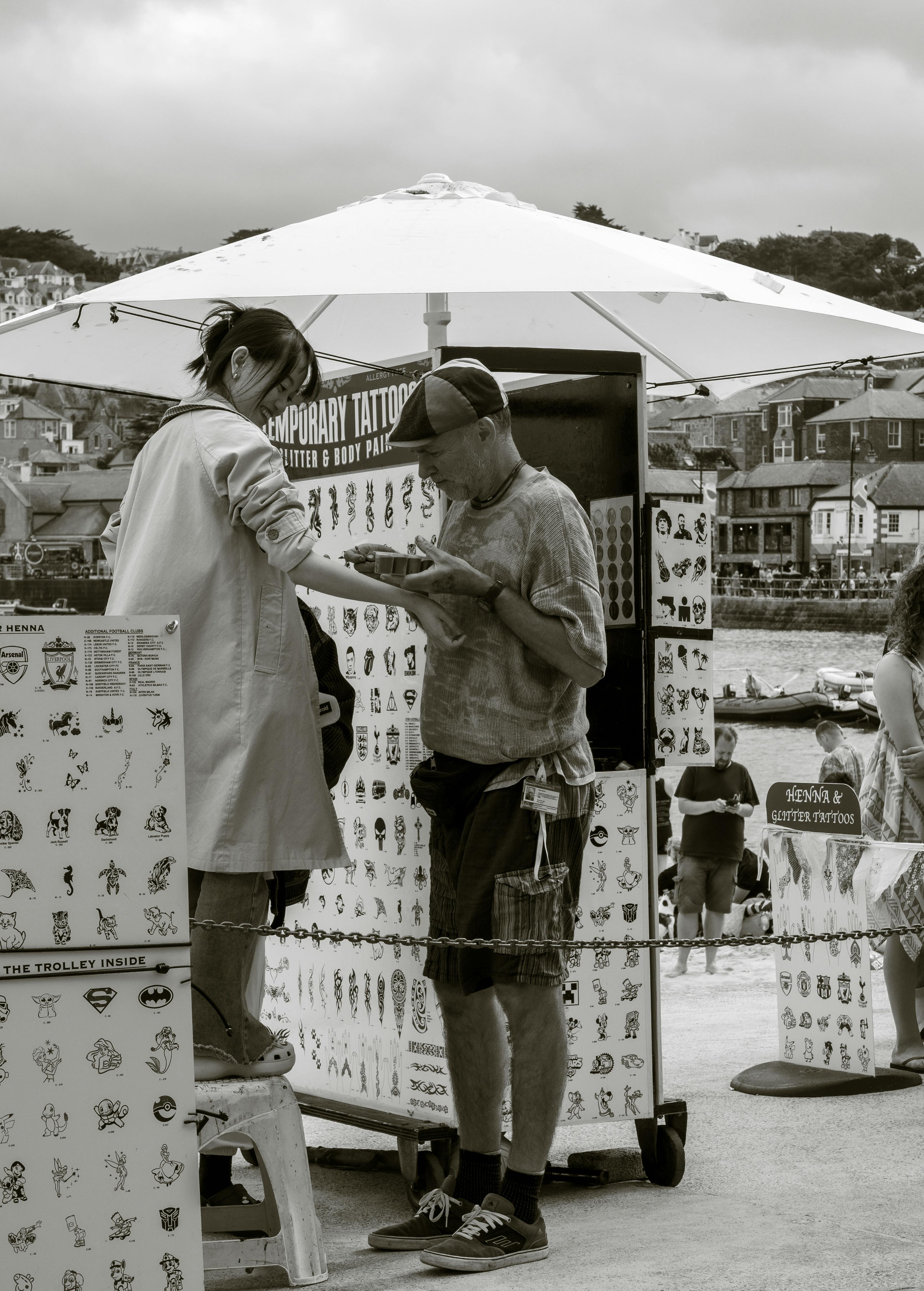 A candid street photo of a temporary tattoo booth with people interacting on a cloudy day.