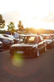 A vintage black car parked at a car gathering during sunset on an open road.