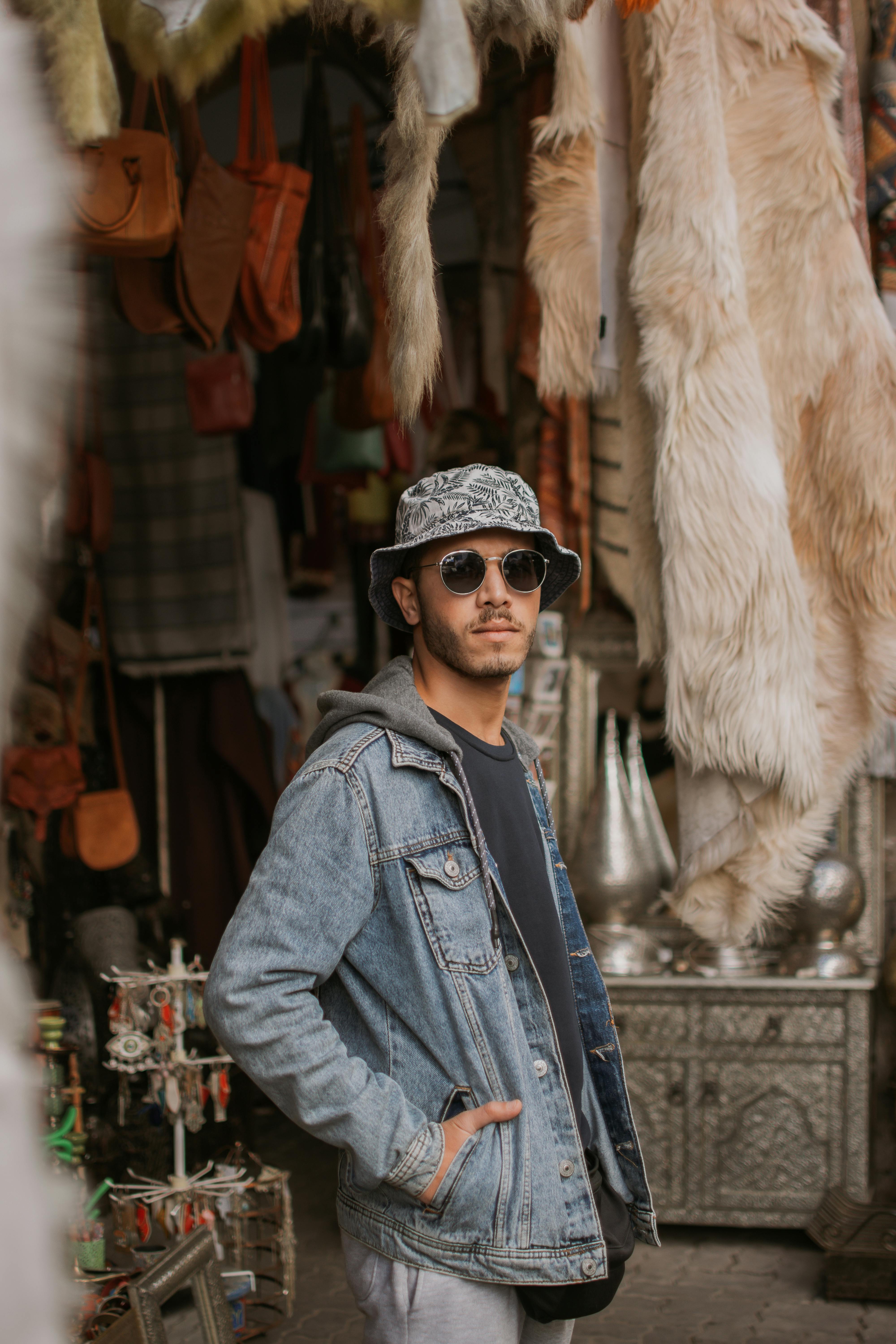 A man in a hat and sunglasses standing in front of a shop