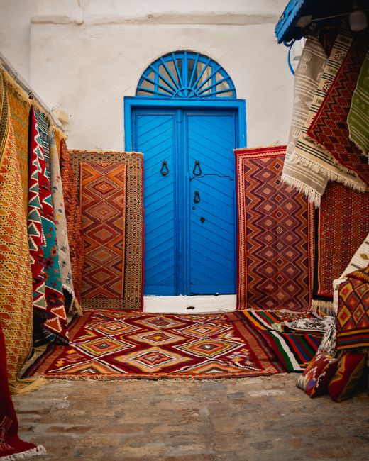 Vibrant display of traditional Tunisian carpets framing a blue door in Carthage.