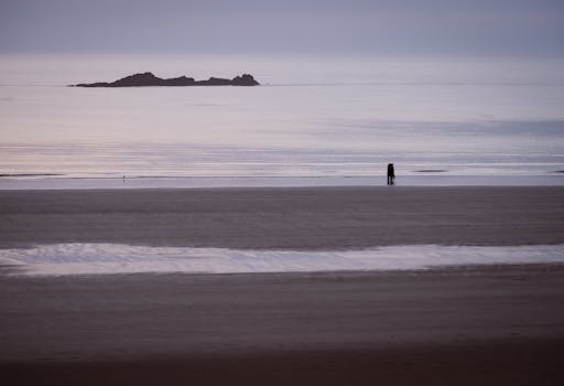 Serene scene of a couple walking on a tranquil beach at low tide in Saint-Malo, Brittany, France.