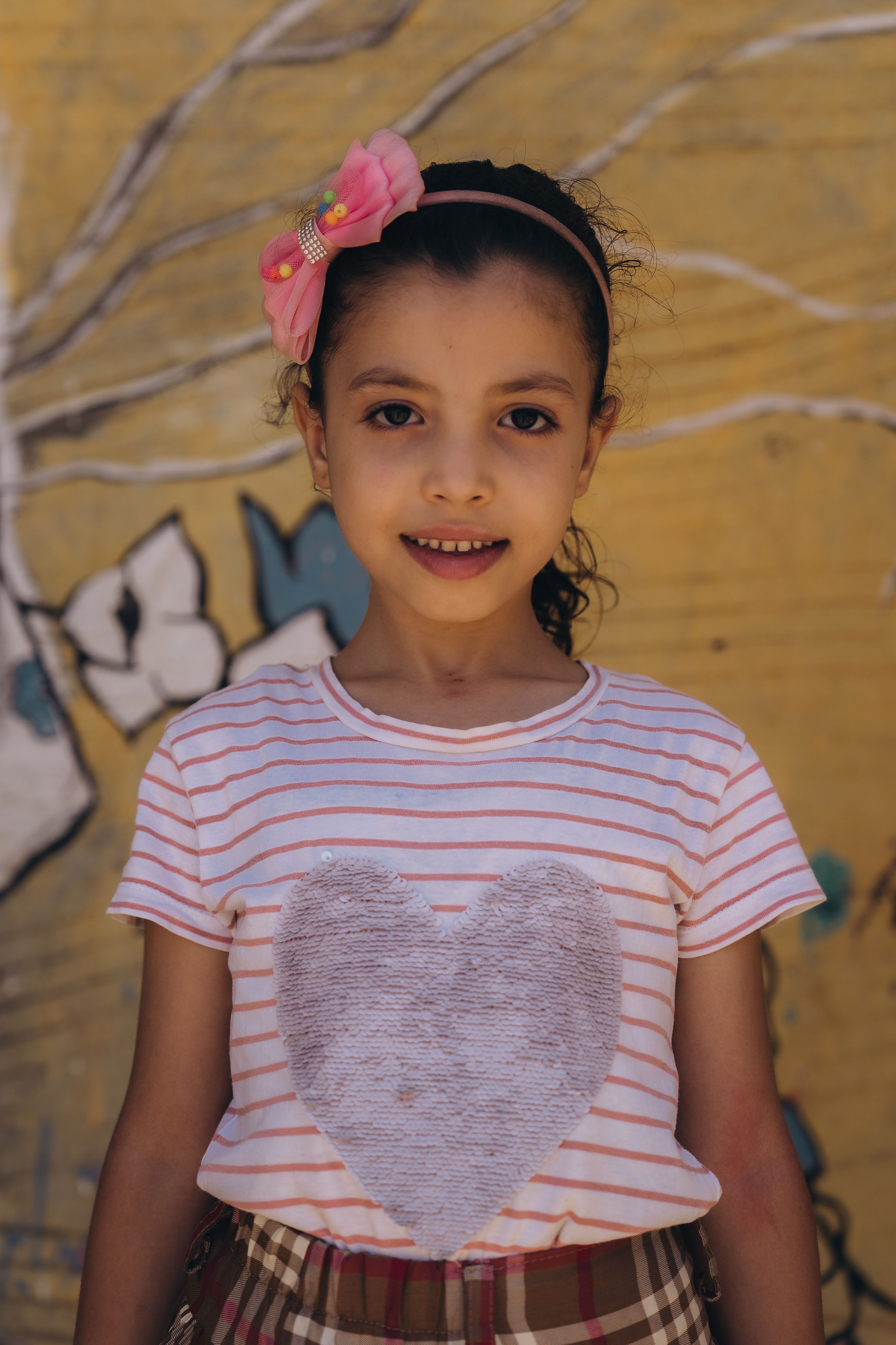 Charming portrait of a young girl smiling against a colorful mural in Kafr El-Shaikh, Egypt.
