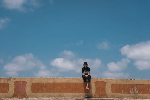 Free A teenager sits alone on a wall against a vibrant blue sky, capturing a moment of solitude and freedom in Egypt. Stock Photo