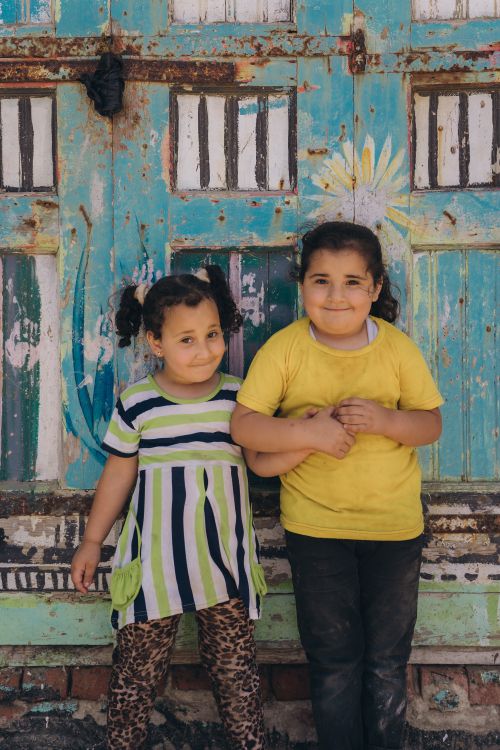 Free Two children smiling in front of a colorful, painted door in Kafr El-Shaikh, Egypt. Stock Photo