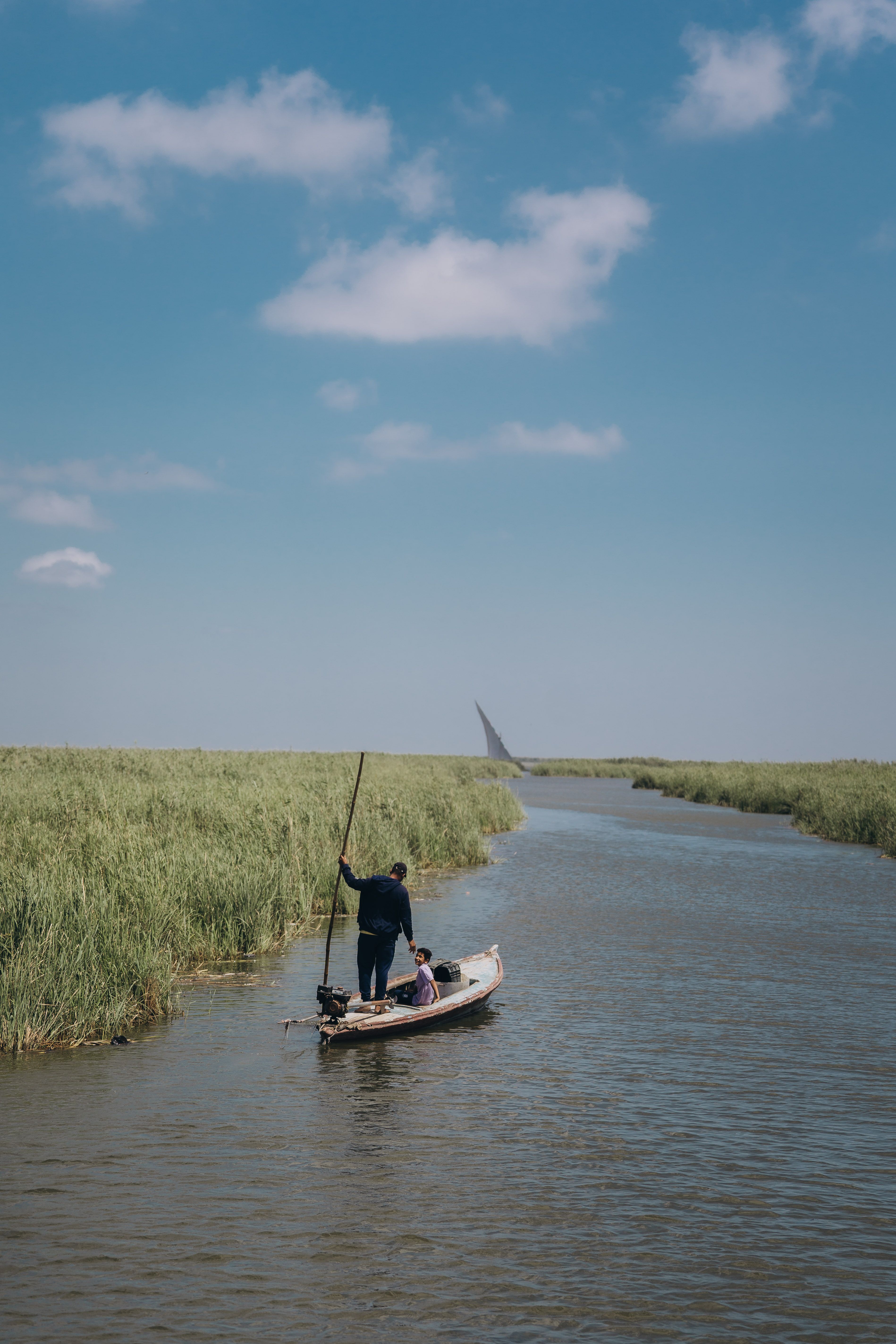 A serene scene of a fisherman on a river in Kafr El-Shaikh, Egypt, under a clear blue sky.