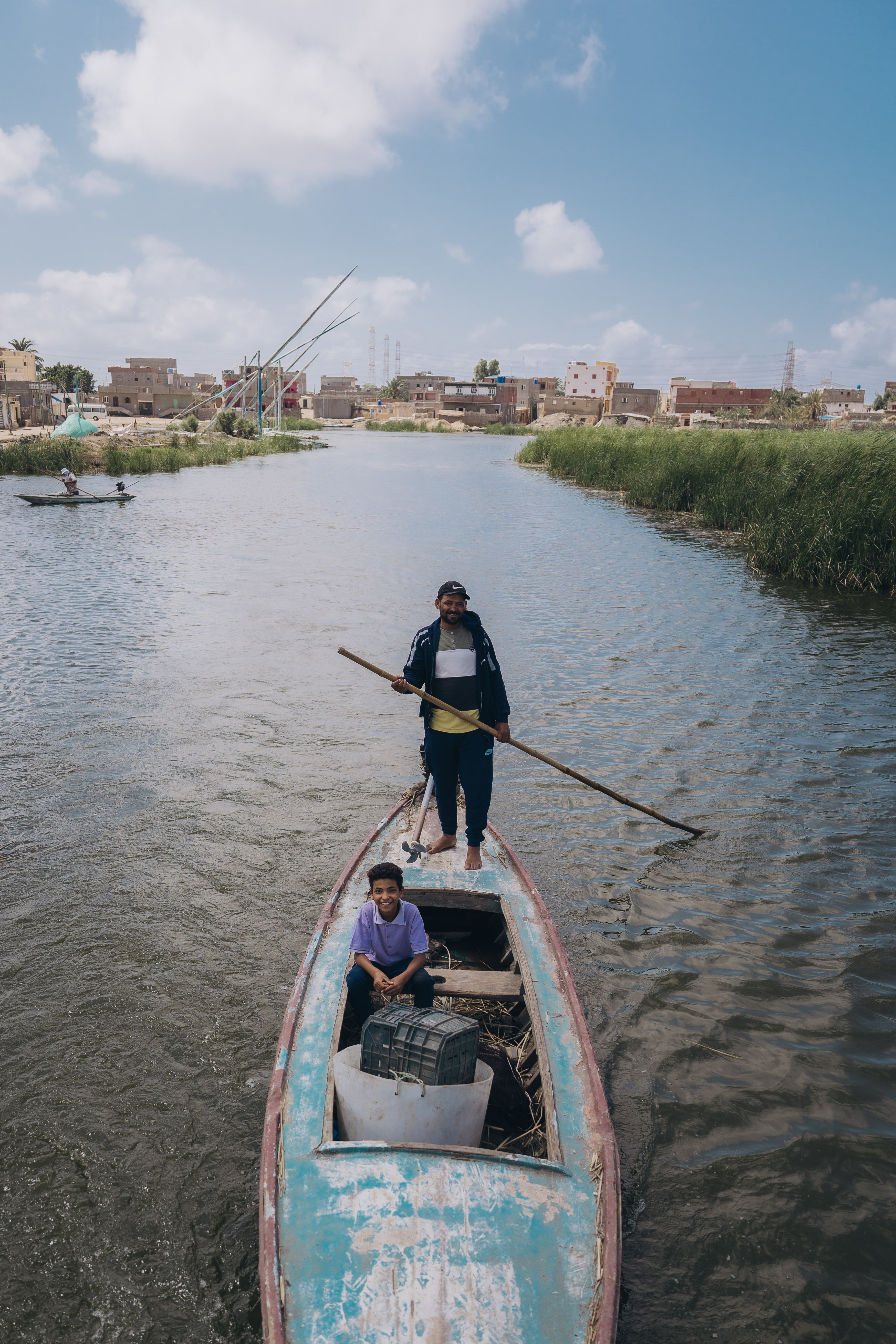 Two fishermen navigating a canal in Kafr El-Shaikh, Egypt on a sunny day.