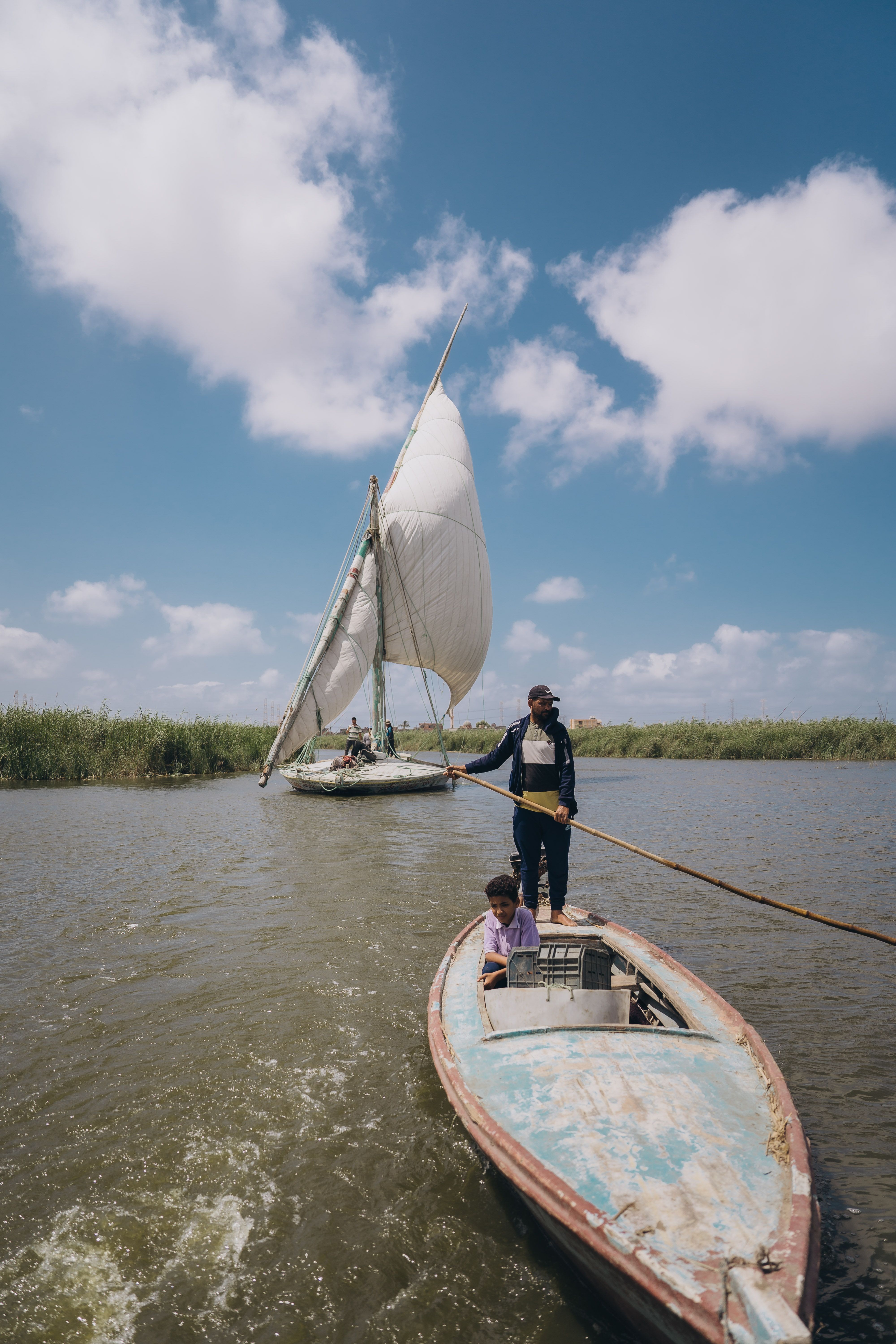 Fishermen on traditional boats in Kafr El-Shaikh, Egypt, under a clear blue sky.