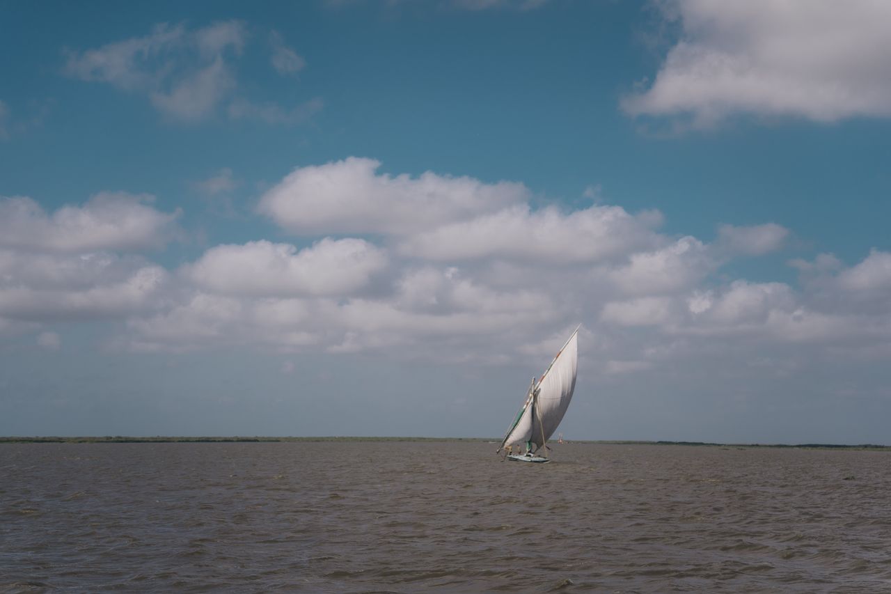 a serene view of a sailboat navigating the calm waters with clouds ove