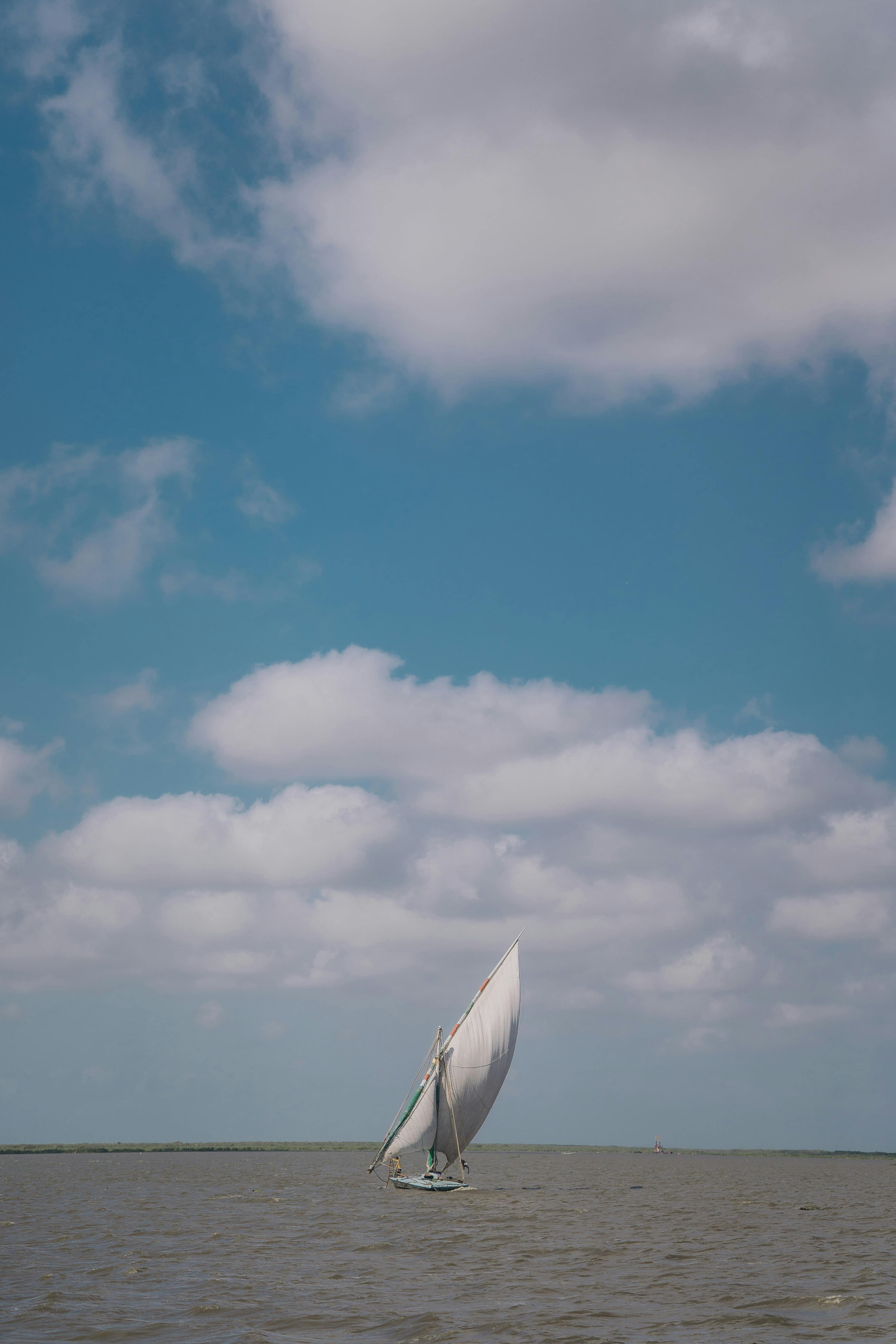 A traditional sailboat gliding on the tranquil sea against a backdrop of blue skies and fluffy clouds.
