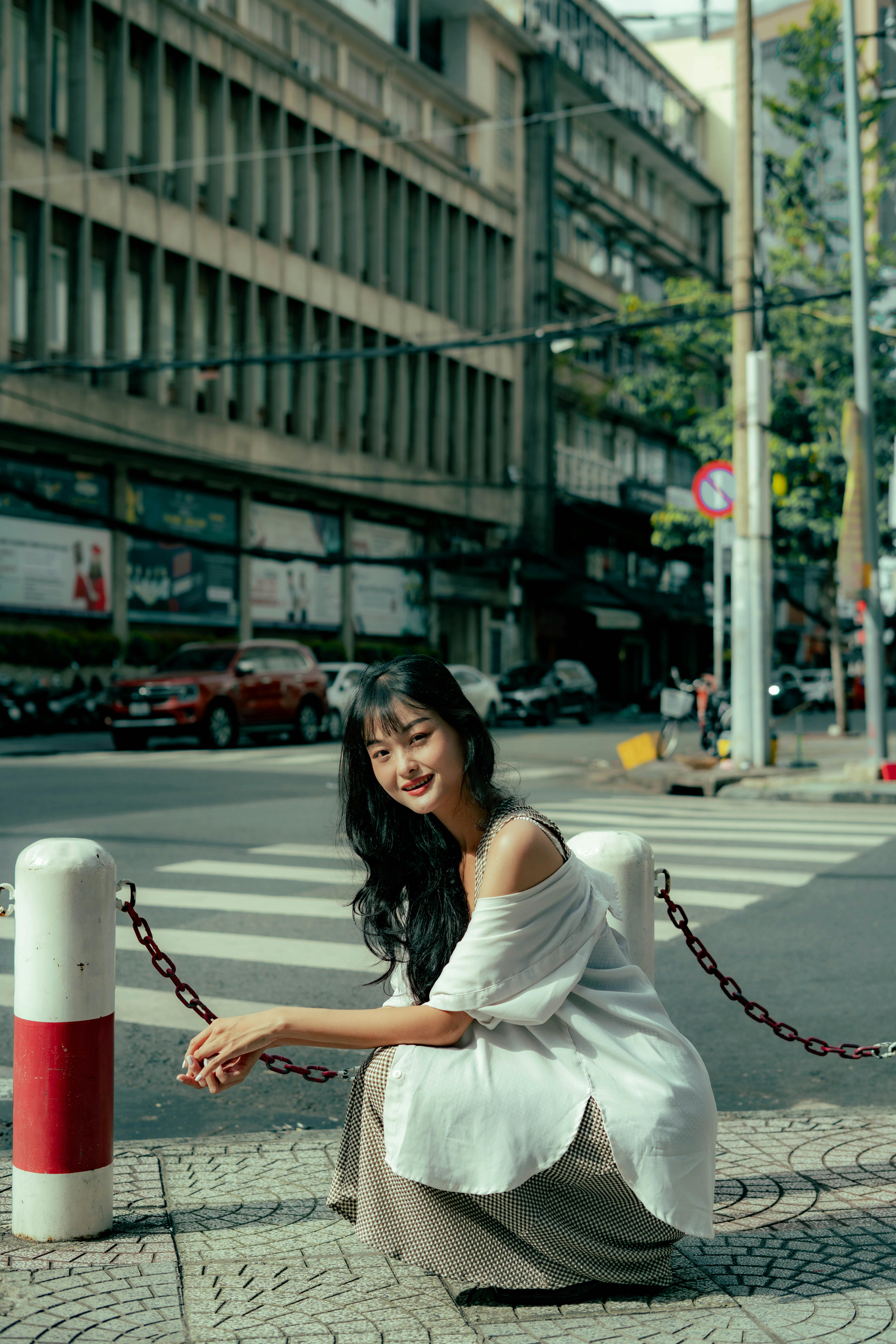 Young woman sitting on a city street corner, embodying relaxed urban style.