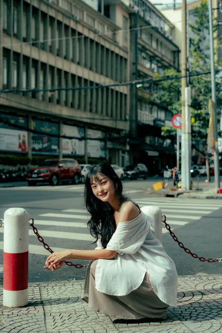 Young woman sitting on a city street corner, embodying relaxed urban style.