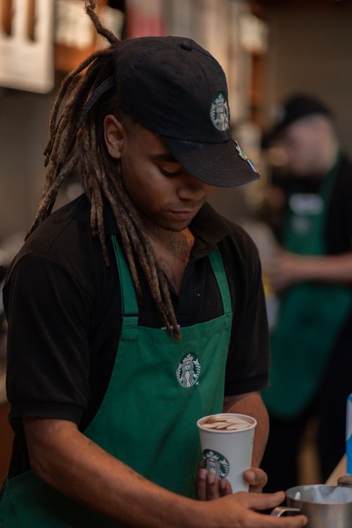 Free Young barista creating a coffee drink in a bustling café environment. Stock Photo
