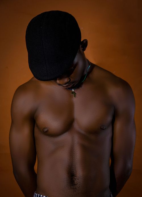 Free Portrait of a fit Black man with defined torso and cap against a warm backdrop, showcasing fitness and style. Stock Photo