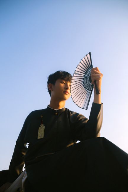 Dramatic portrait of a man holding a hand fan against a clear sky.