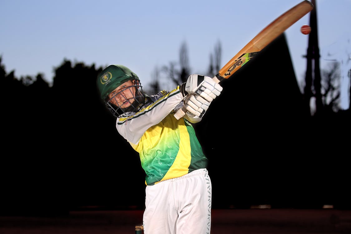 A young man in a green and yellow uniform swinging a bat · Free Stock Photo
