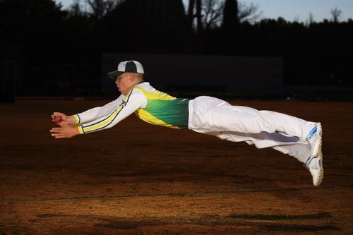Free Cricketer in full sports gear leaps through the air to catch the ball, showing athleticism and focus. Stock Photo