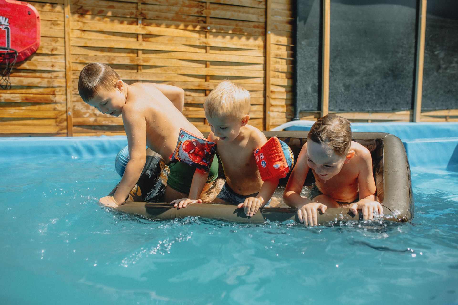 Three boys playing in a pool with an inflatable raft