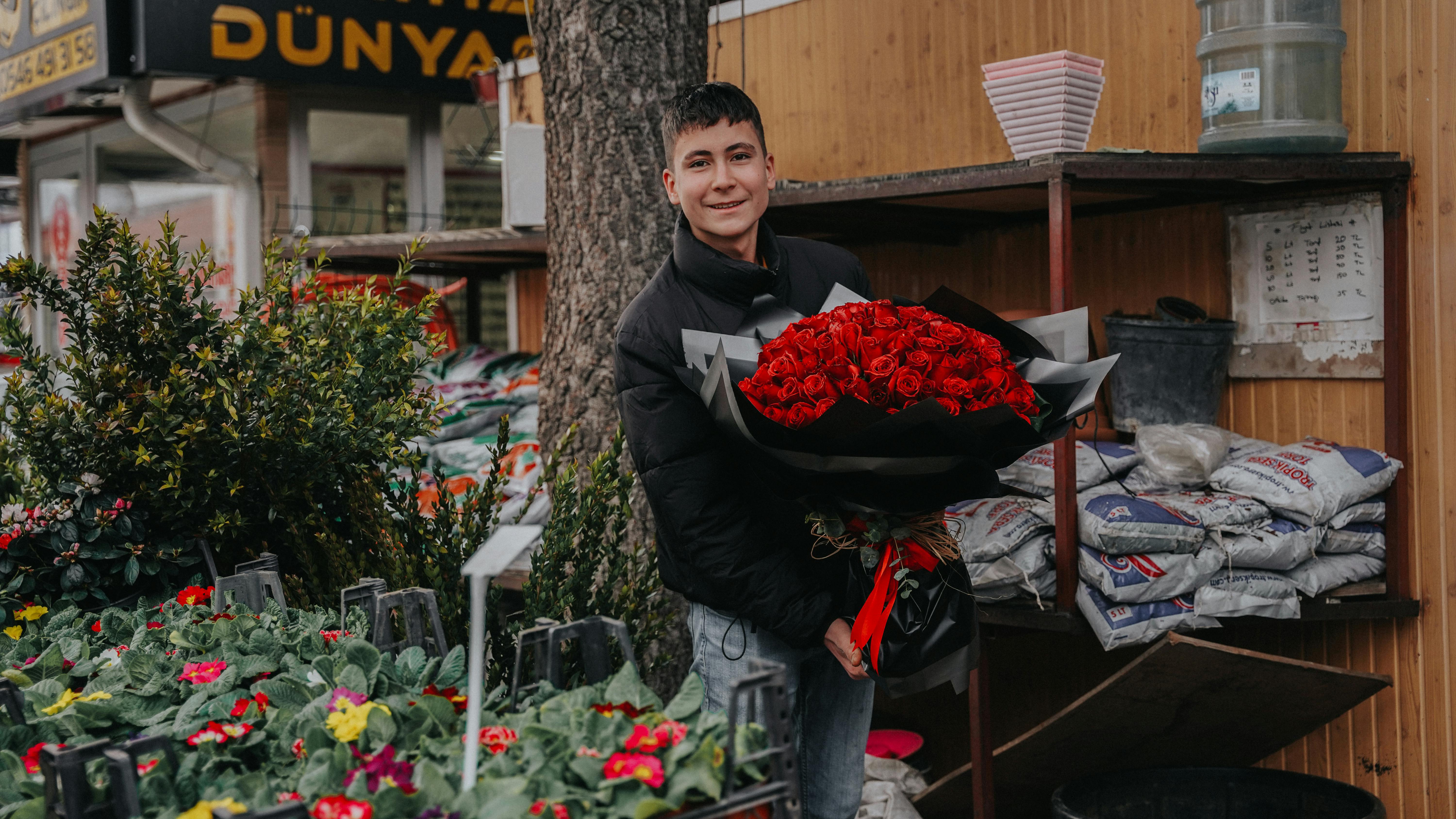 A man holds a large bouquet of red roses in an outdoor market in Isparta, Türkiye.