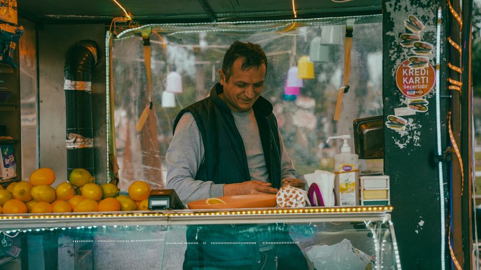 Man at fruit stall in Isparta, Türkiye, preparing produce for sale, surrounded by vibrant colors.