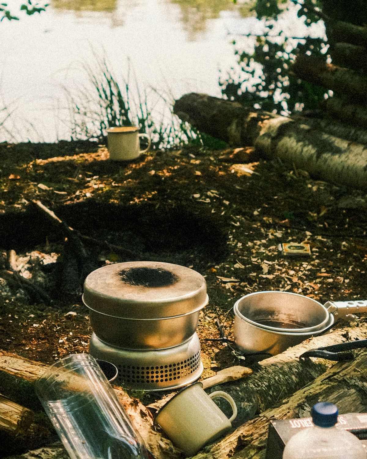 Camping cookware and stove arranged beside a lake