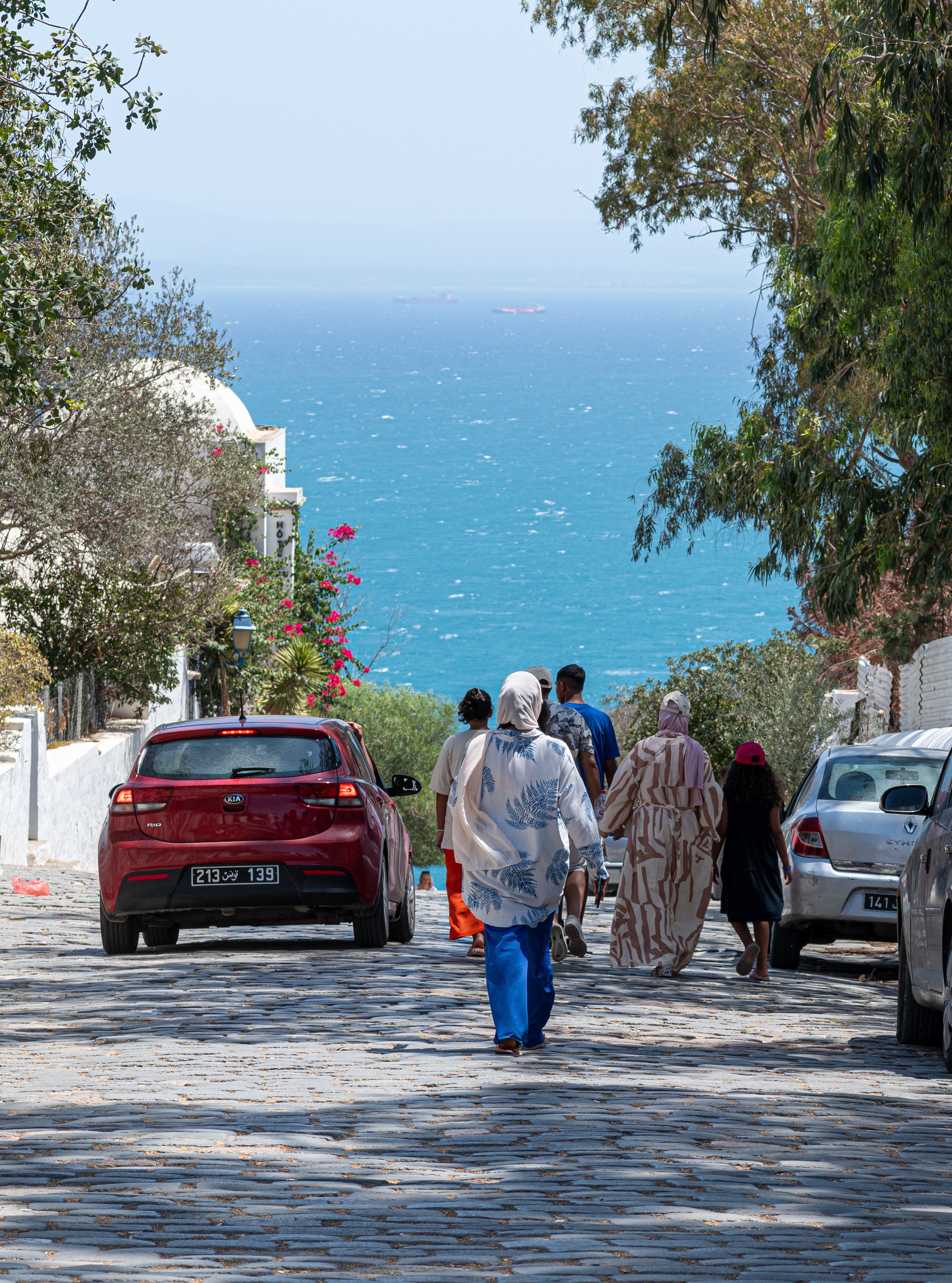 Charming view of people on a cobbled street in Carthage, Tunisia, with the sea in the distance.