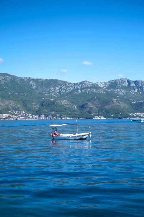 Free Peaceful scene of a boat floating on a tranquil lake surrounded by mountains and blue skies. Stock Photo