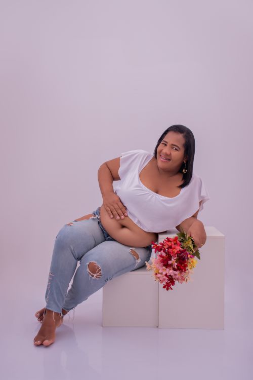 Free Pregnant woman sitting joyfully with flowers in a bright studio setting. Stock Photo