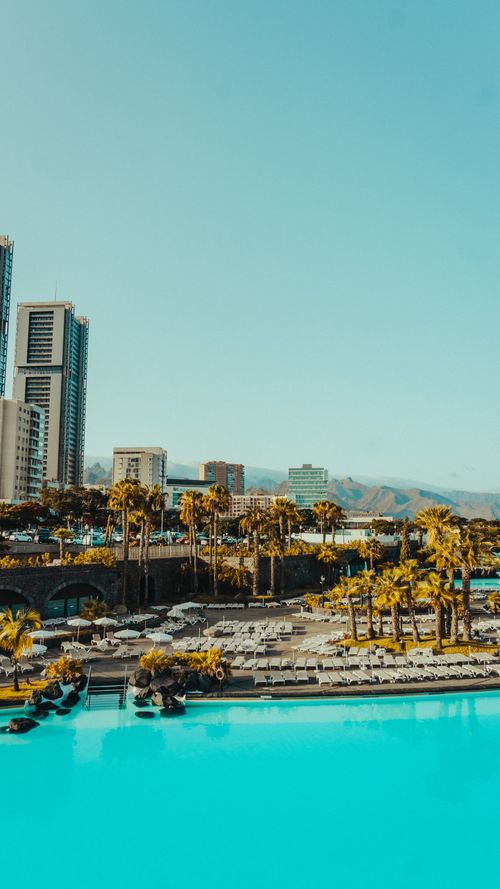 Free A vibrant cityscape featuring a pool, palm trees, and towering buildings under a clear blue sky. Stock Photo