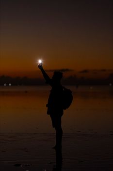 Silhouette of person taking a photo with a phone during sunset on the beach, creating a serene and peaceful scene.