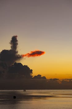Vibrant sunset over a calm sea with dramatic cloud formations in a serene seascape.