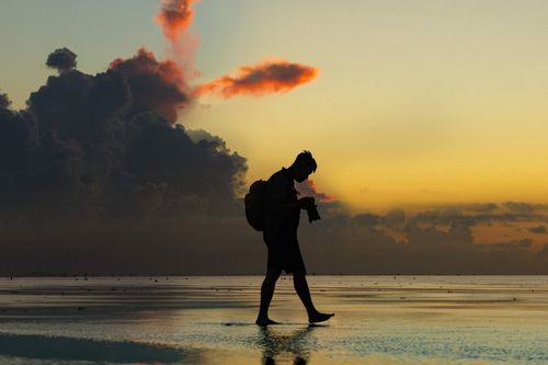 Free Silhouette of a person walking along a beach during a stunning sunset with dramatic clouds. Stock Photo