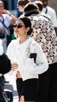 Woman in stylish white sweater and sunglasses at outdoor fashion event.