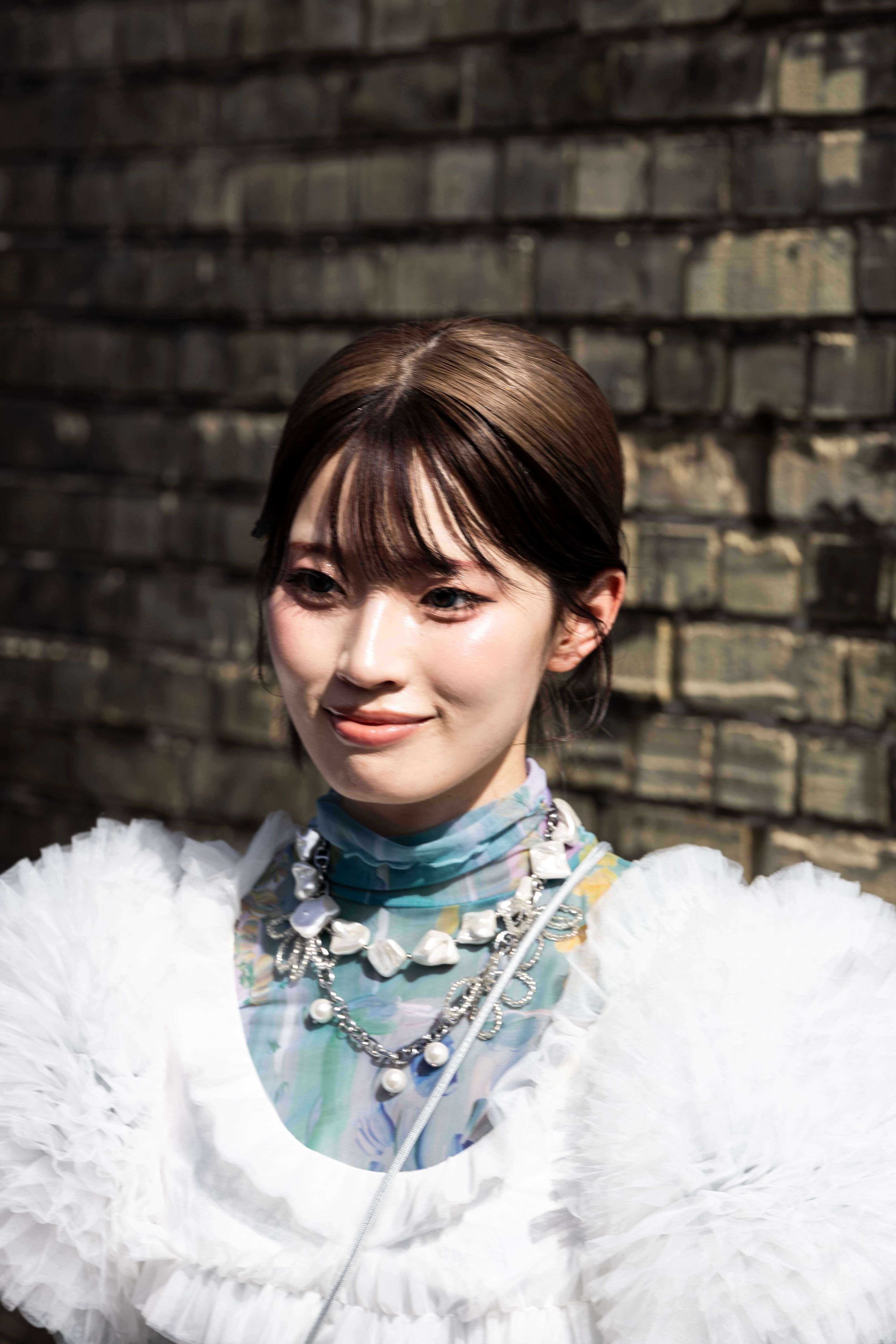 Elegant woman poses in a fashionable white outfit against a brick wall, showcasing her unique style.