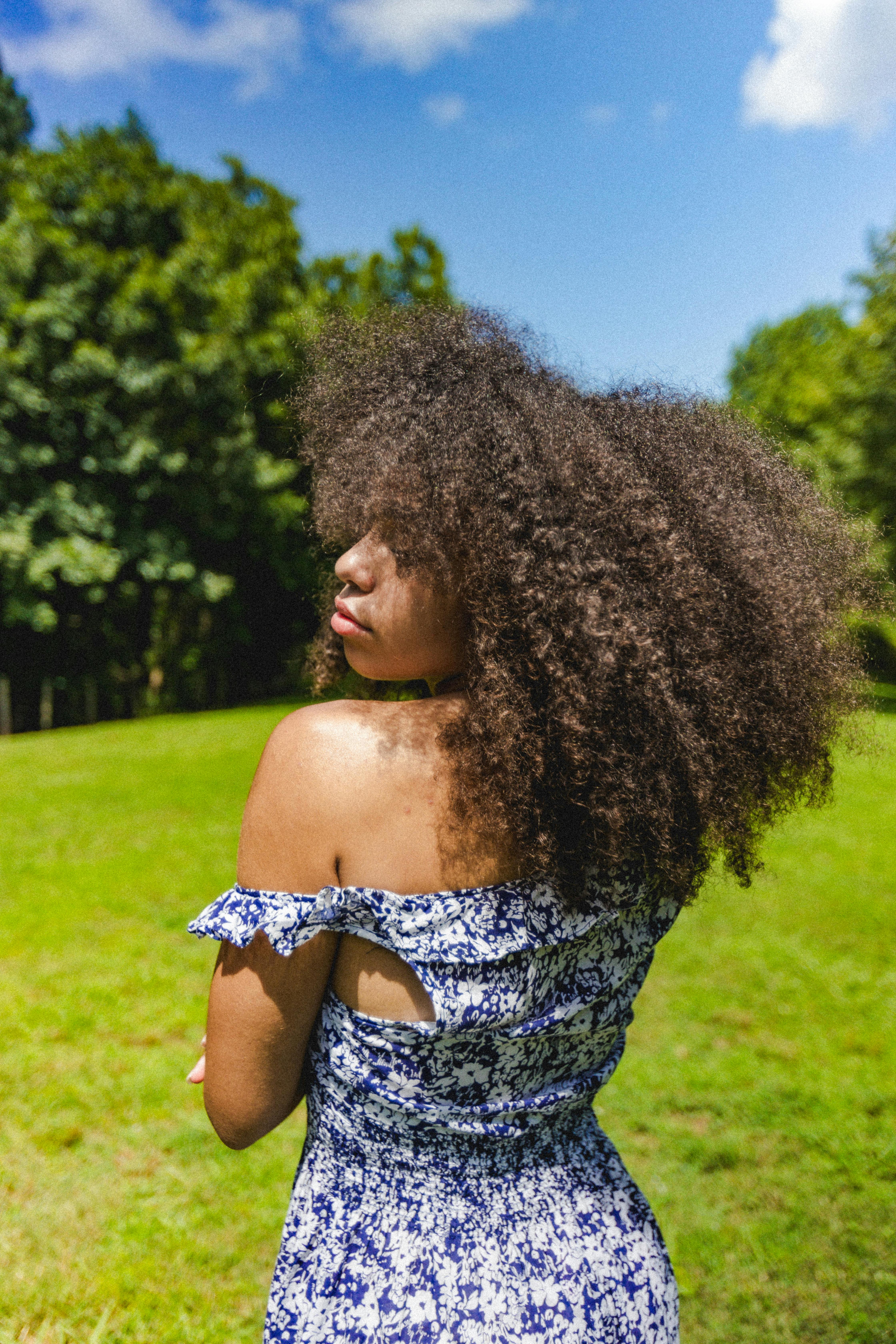 A woman with curly hair in a blue dress enjoys a sunny day in an Atlanta park.