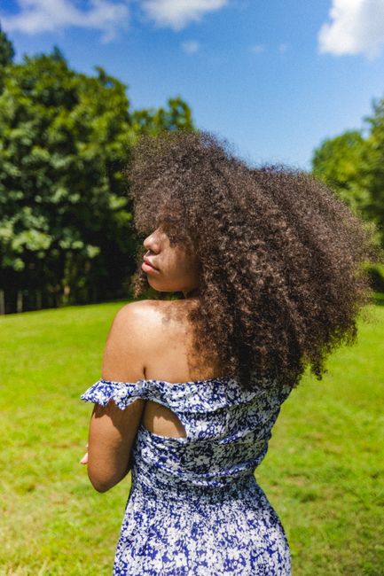 A woman with curly hair in a blue dress enjoys a sunny day in an Atlanta park.