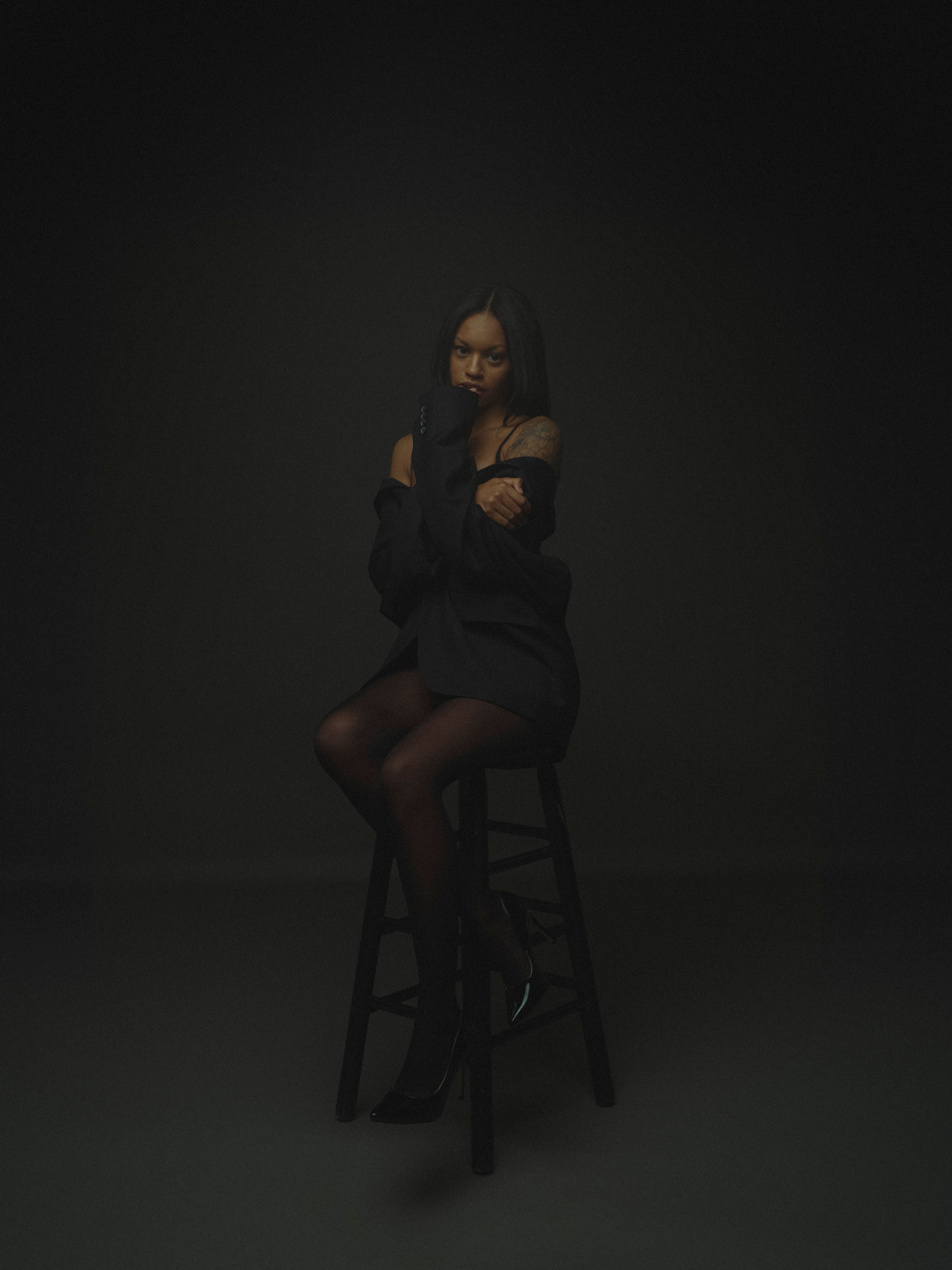 A woman sitting on a stool in a dark room · Free Stock Photo