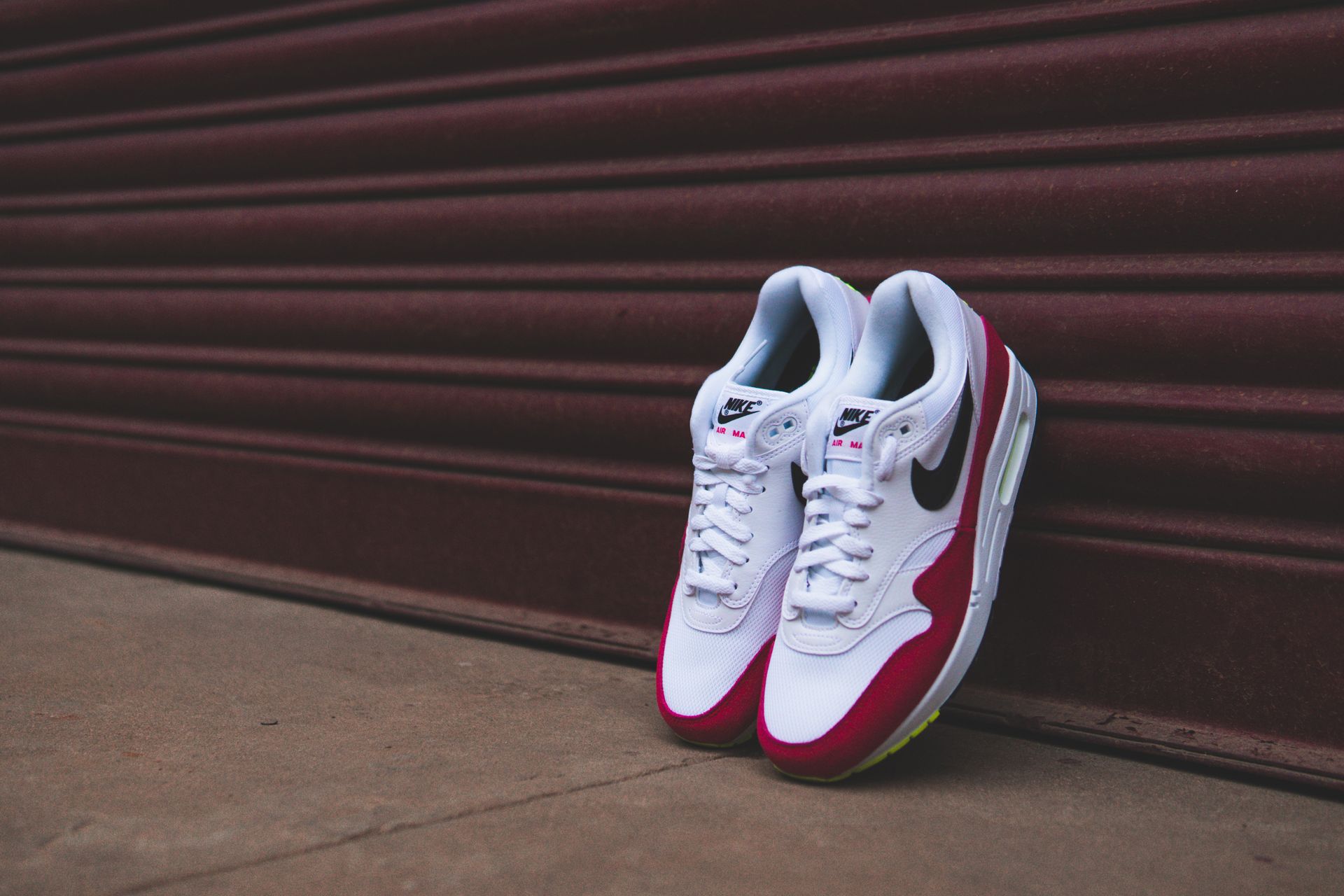 Stylish white and red sneakers leaning against a closed metal shutter, showcasing footwear design.