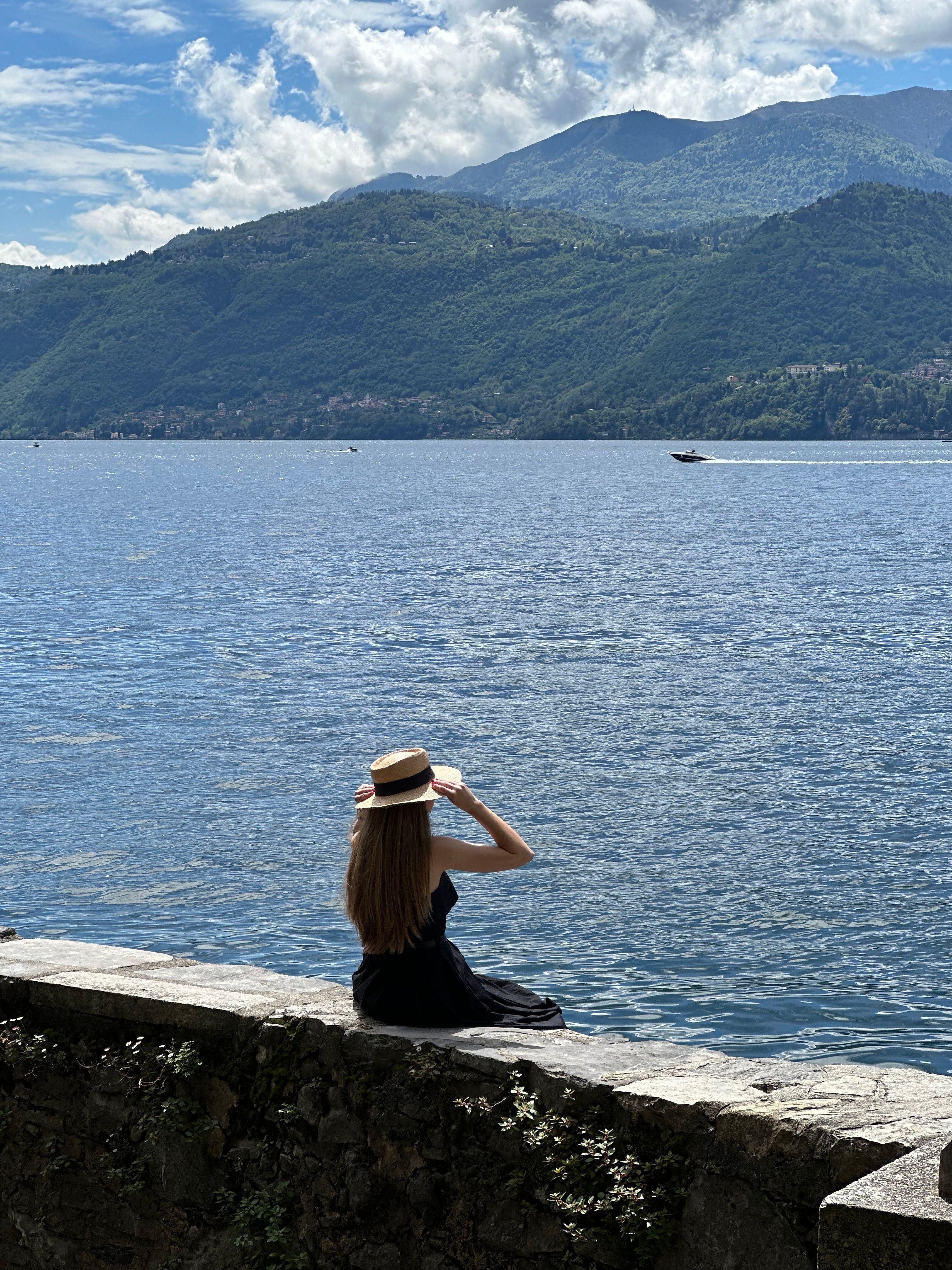 A woman sitting on a wall looking out over the water · Free Stock Photo