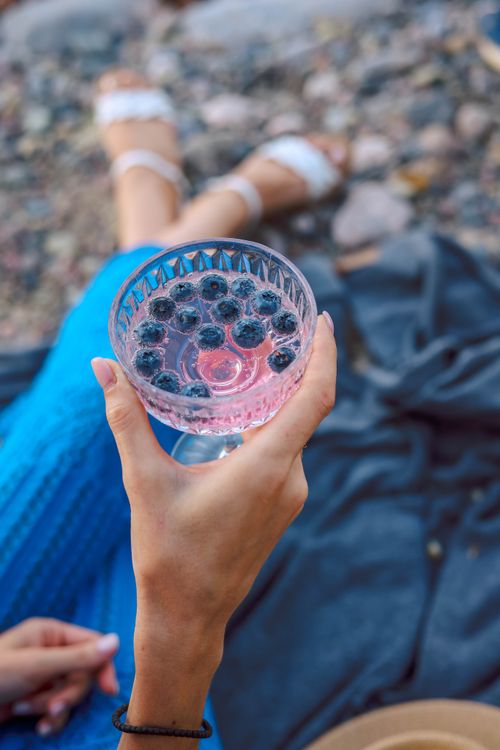 Free Hand holding a blueberry-infused summer cocktail by the beach. Stock Photo