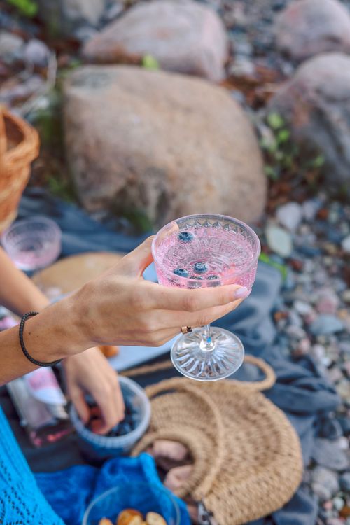 Free Woman holding a refreshing drink during a summer picnic outdoors on a rocky beach. Stock Photo