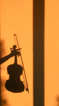 Silhouette of a hand holding a violin against a vibrant orange wall.