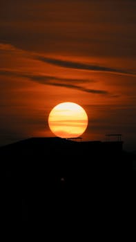 Sunset view with silhouette skyline, large sun and warm orange tones.